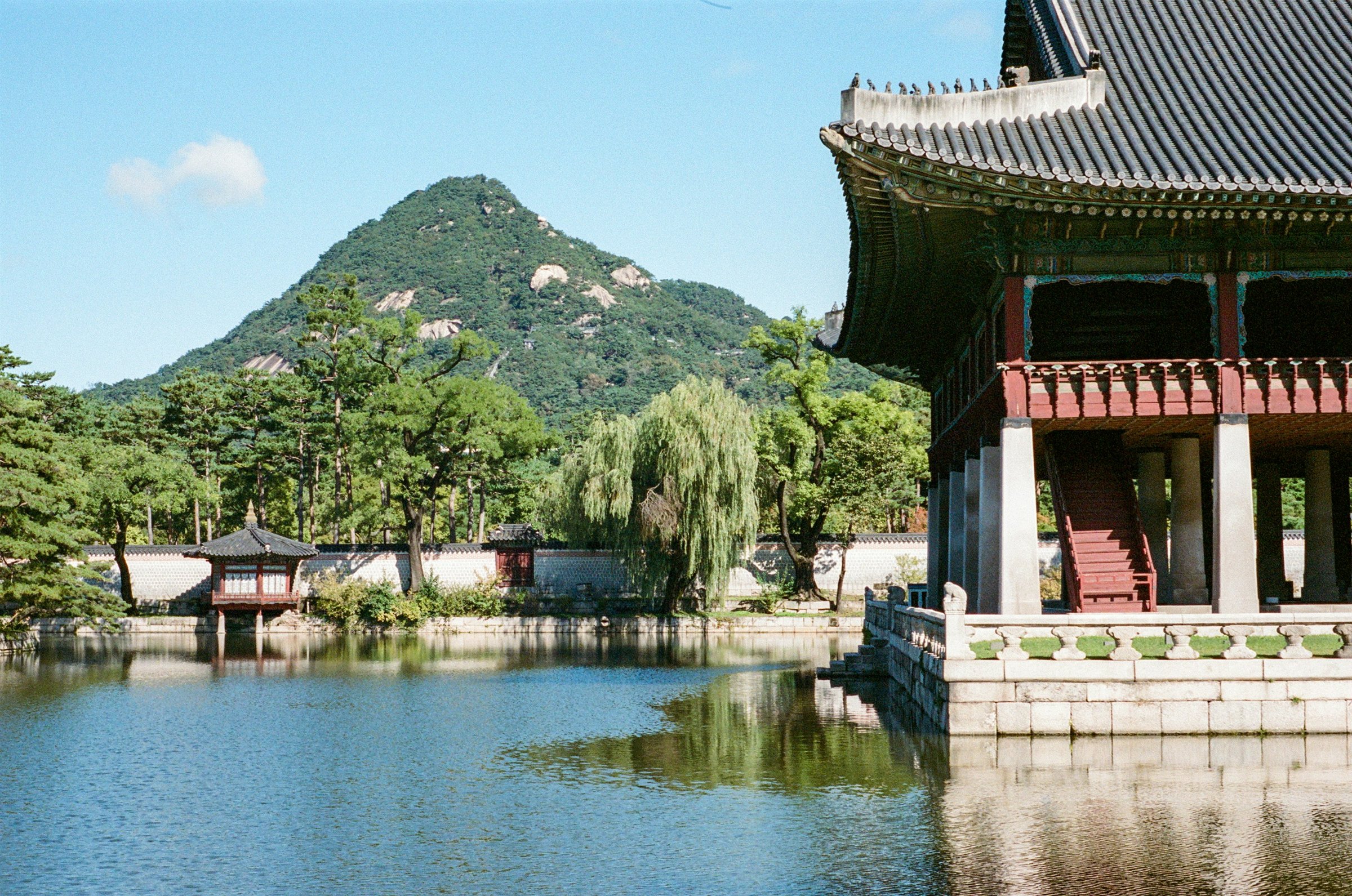 A palace beside a still pond, with green mountains behind it in Seoul